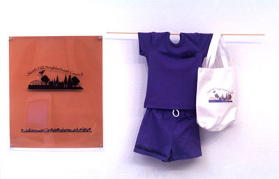 Image of North Hill Neighborhood Council Logo display at my BFA show: logos have been applied to a t-shirt, a pair of shorts, and a bag.
